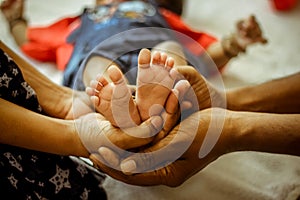 Parenthood Concept - Happy Mom and Dad are holding Baby feet on hands. Parents are holding the legs of a newborn baby