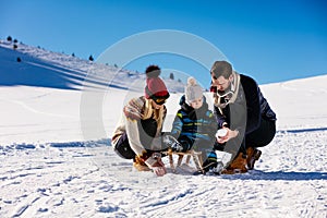 Parenthood, fashion, season and people concept - happy family with child on sled walking in winter outdoors