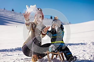 Parenthood, fashion, season and people concept - happy family with child on sled walking in winter outdoors