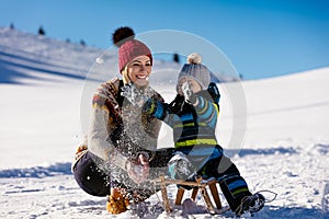 Parenthood, fashion, season and people concept - happy family with child on sled walking in winter outdoors