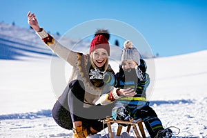 Parenthood, fashion, season and people concept - happy family with child on sled walking in winter outdoors