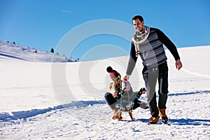 Parenthood, fashion, season and people concept - happy family with child on sled walking in winter outdoors