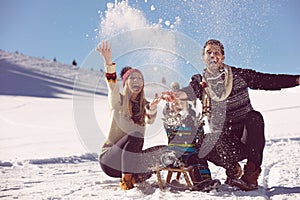Parenthood, fashion, season and people concept - happy family with child on sled walking in winter outdoors