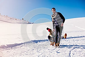 Parenthood, fashion, season and people concept - happy family with child on sled walking in winter outdoors