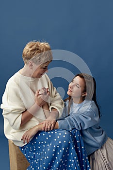 Parenthood support. Portrait of middle-aged woman and her young daughter posing over blue studio background. Concept of