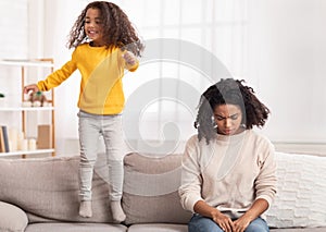 Exhausted Mother Sleeping While Hyperactive Daughter Jumping On Sofa Indoor