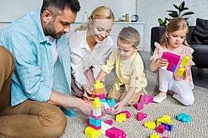 parents with adorable little children playing with colorful blocks at home