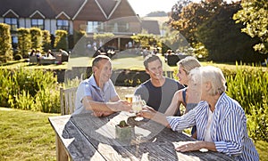 Parents With Adult Offspring Enjoying Outdoor Summer Drink At Pub