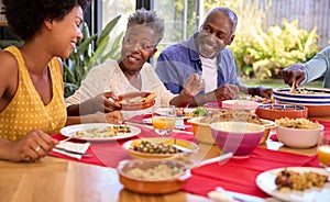 Parents With Adult Offspring Sitting Around Table At Home Enjoying Meal Together