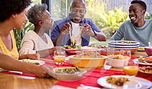 Parents With Adult Offspring Sitting Around Table At Home Enjoying Meal Together