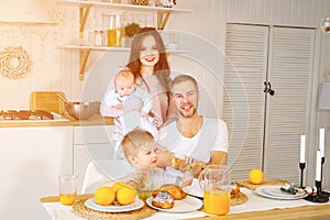 Parents with baby and funny boy smiling and while enjoying buns and juice for breakfast together