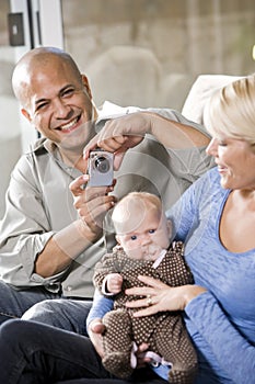 Parents with baby at home, dad holding camera