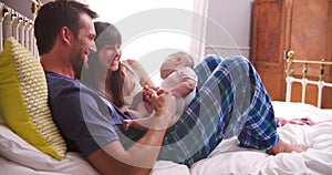 Parents In Bed Playing With Newborn Baby Daughter