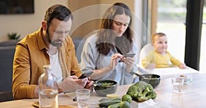 Parents busy in their phones during a lunch with their baby son