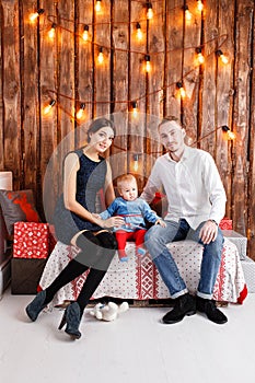 Parents and child having fun in loft-style room, wooden rustic background with a garland of bulbs. Loving family Merry