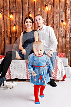 Parents and child having fun in loft-style room, wooden rustic background with a garland of bulbs. Loving family Merry