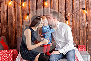 Parents and child having fun in loft-style room, wooden rustic background with a garland of bulbs. Loving family Merry