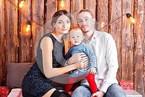 Parents and child having fun in loft-style room, wooden rustic background with a garland of bulbs. Loving family Merry