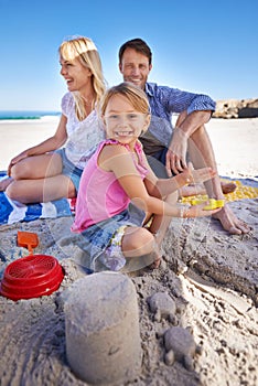 Parents, child and sandcastle in portrait at beach, blanket and excited with smile for holiday in summer. Father, mother