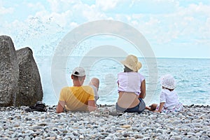 Parents with child sit on seacoast, rear view