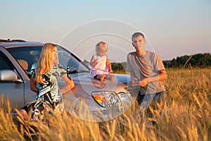 Parents and child sitting on car cowl on wheaten f