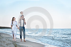 Parents and child walking at ocean shore at sunset. Vacation at sea with children