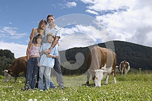 Parents with children (7-9) embracing in field with cows portrait