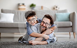 Parents and children being friends. Joyful father and son having fun, dad lying on floor, carrying boy on back