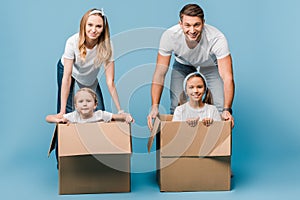 Parents with children in cardboard boxes for relocation on blue