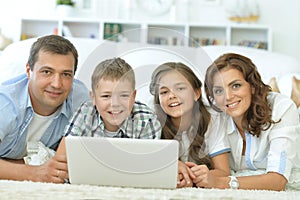 parents with children with laptops are lying on the carpet