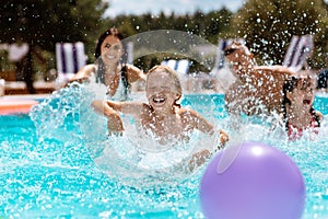 Parents and children laughing while playing ball in swimming pool