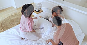 Parents, children and pillow fight in bed in morning, playing and care to love together. Mom, dad or kids for funny game