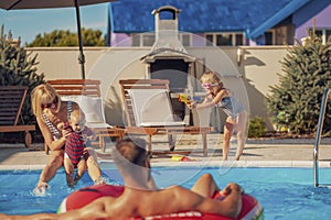 Parents and children playing with squirt guns by the pool