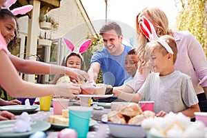 Parents With Children Wearing Bunny Ears Enjoying Outdoor Easter Party In Garden At Home