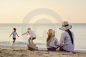 Parents and children who enjoy a picnic at the beach on sunset in holiday