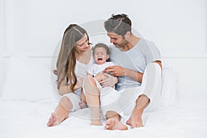 Parents with crying baby sitting on bed