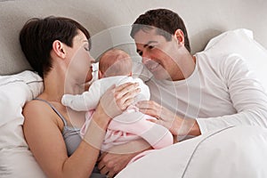 Parents Cuddling Newborn Baby In Bed