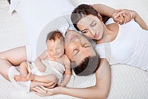 Parents cuddling newborn baby in bed at home. Mom, dad and baby.