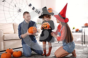 Parents and cute little girl with pumpkin candy bucket at Halloween party