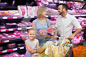 Parents with daughter choosing meat in refrigerated section in h