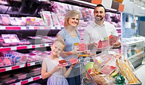 Parents with daughter choosing meat in refrigerated section in hypermarket