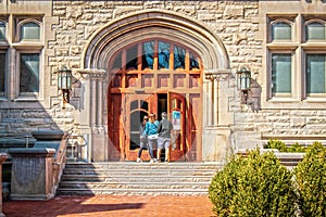 Parents and female student entering large arched doors of University building flanked by metal gothic lamps