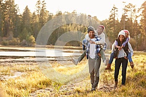 Parents Giving Children Piggyback Ride On Walk By Lake