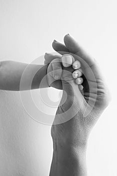 Parents' hands hold the fingers of a newborn baby. Tiny fingers in a black white