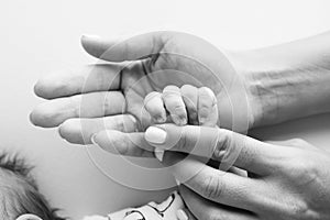 Parents& x27; hands hold the fingers of a newborn baby. Tiny fingers in a black white