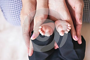 Parents hands holding little baby boy feet, view from above