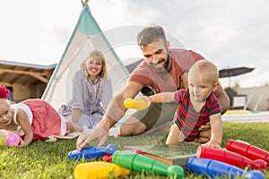 Parents having fun playing bowling with little children while camping in the backyard