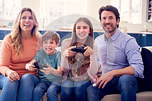 Parents Having Fun Sitting On Sofa With Children At Home Playing On Games Console