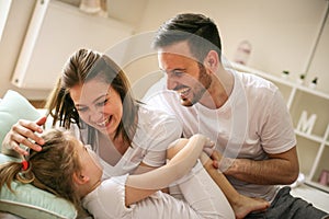 Parents having fun with their little daughter on bed.