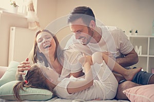 Parents having fun with their little daughter on bed.